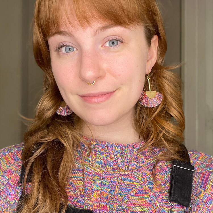 A photo of the artist! Jordan is seen here smiling with a pair of colorful earrings and a matching sweater.