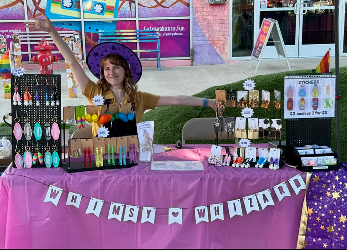 A photo of the artist! Jordan is seen here smiling with a pair of colorful earrings and a matching sweater.