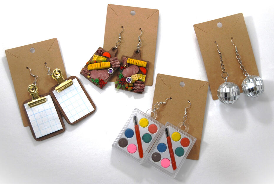 Four pairs of earrings made by Jordan. The first are small tiny functional clipboards, the second look like charcuterie boards, the third is a pair of miniature watercolor palettes, and the last are little disco balls!